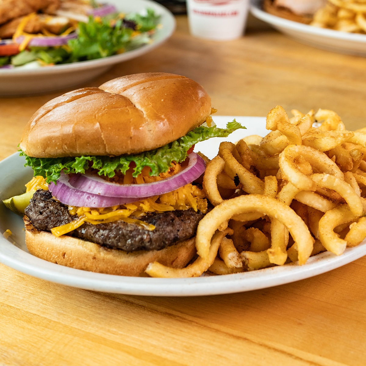 Juicy Oklahoma BBQ burger topped with fresh lettuce, sliced red onions, and melted cheddar cheese, served with a side of crispy curly fries at Earl's Rib Palace.