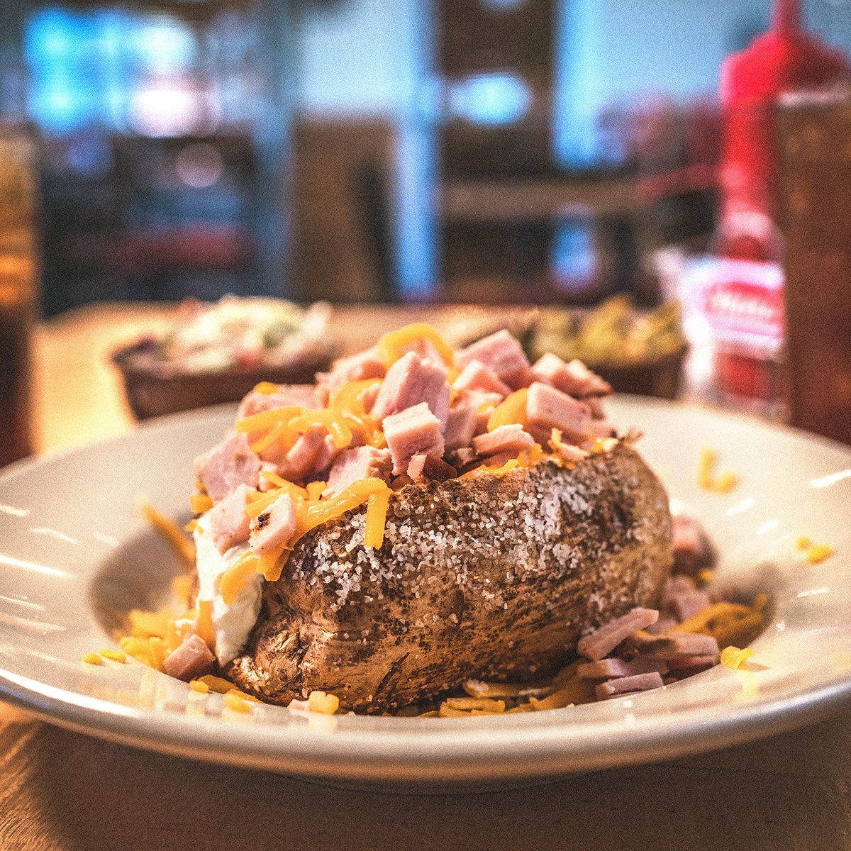 Baked potato topped with savory ham and shredded cheddar cheese, served at Earl's Rib Palace, a premier destination for Oklahoma BBQ. Enjoy this hearty side dish alongside your favorite BBQ meal.